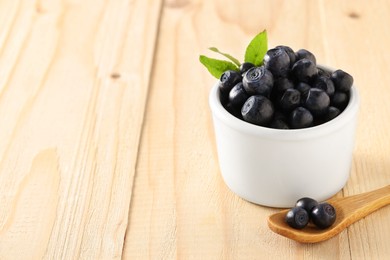 Photo of Bowl and spoon with tasty fresh bilberries on wooden table, space for text