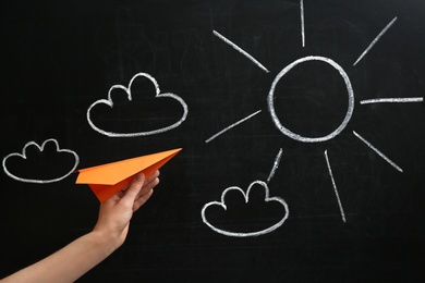 Photo of Woman holding paper plane near blackboard, closeup