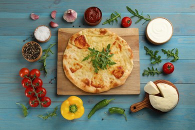 Photo of Delicious khachapuri with cheese surrounded by different products on light blue wooden table, flat lay