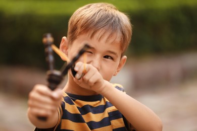 Photo of Little boy playing with slingshot in park