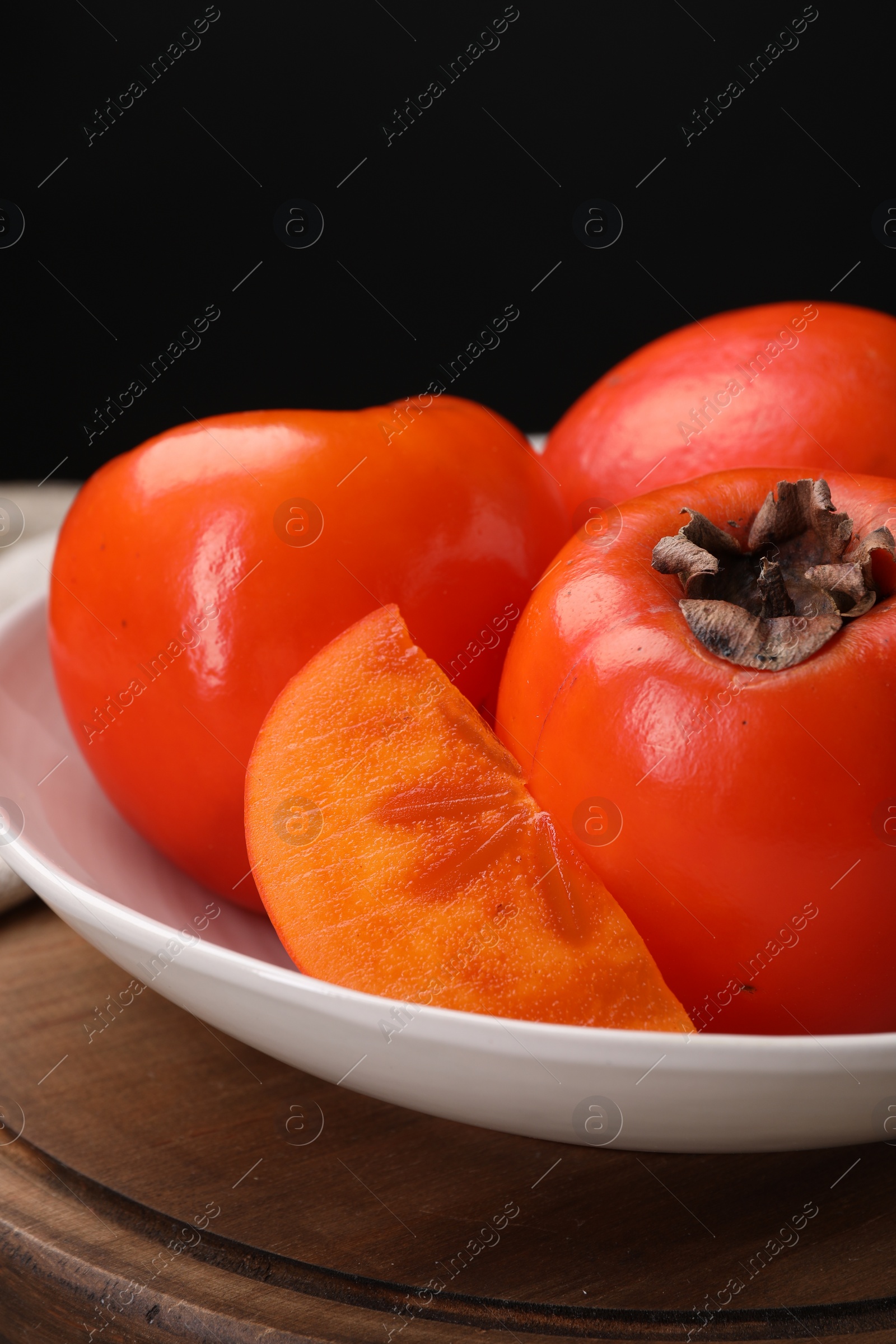 Photo of Delicious ripe persimmons on wooden board, closeup