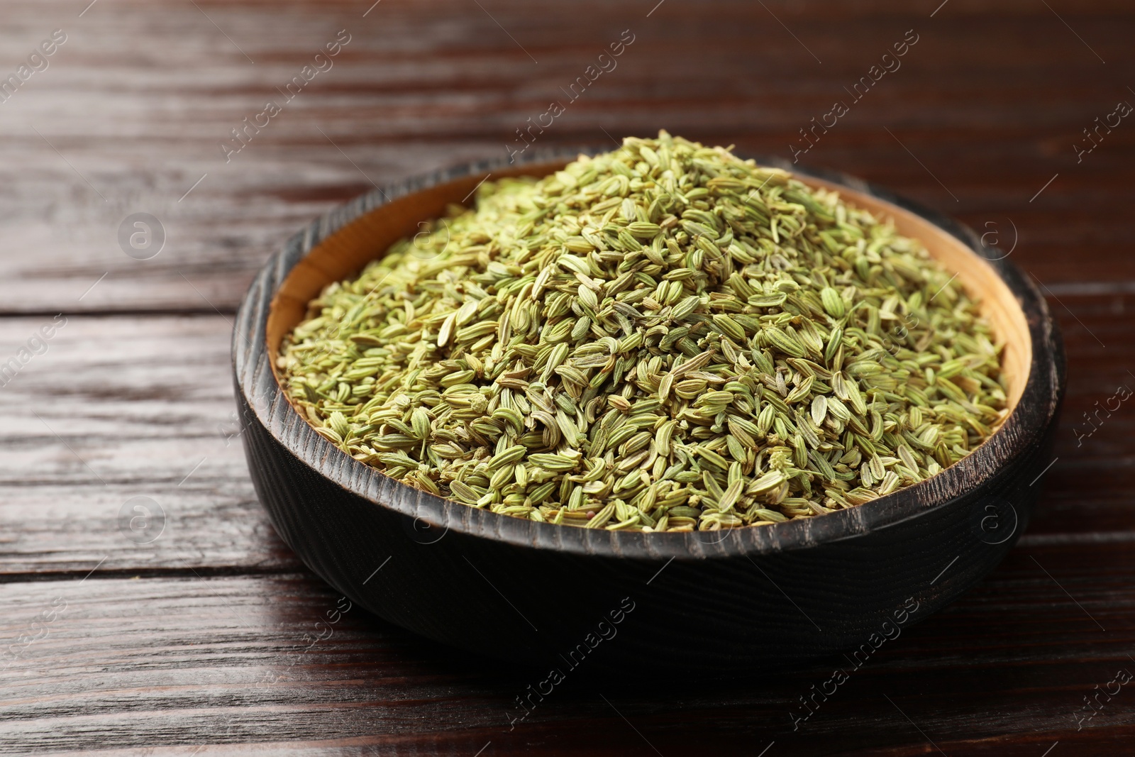 Photo of Fennel seeds in bowl on wooden table, closeup