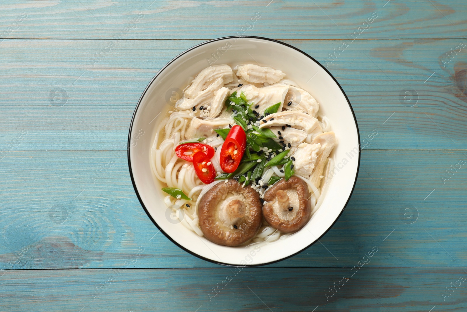 Photo of Delicious ramen with meat and mushrooms in bowl on light blue wooden table, top view. Noodle soup