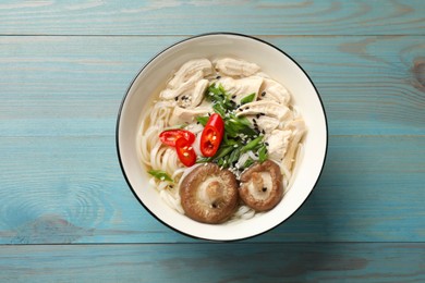 Photo of Delicious ramen with meat and mushrooms in bowl on light blue wooden table, top view. Noodle soup