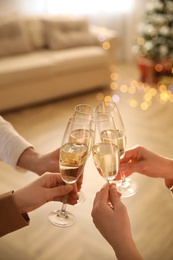 Photo of People clinking glasses of champagne in room decorated for Christmas, closeup. Holiday cheer and drink