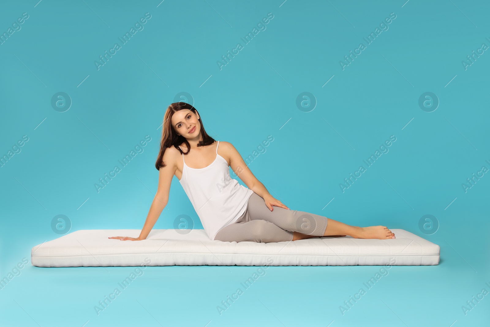 Photo of Young woman sitting on soft mattress against light blue background