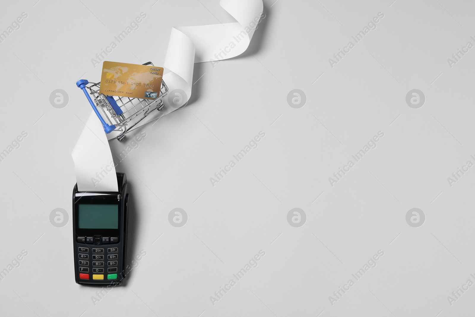 Photo of Payment terminal with thermal paper for receipt, small shopping cart and credit card on light grey background, flat lay. Space for text