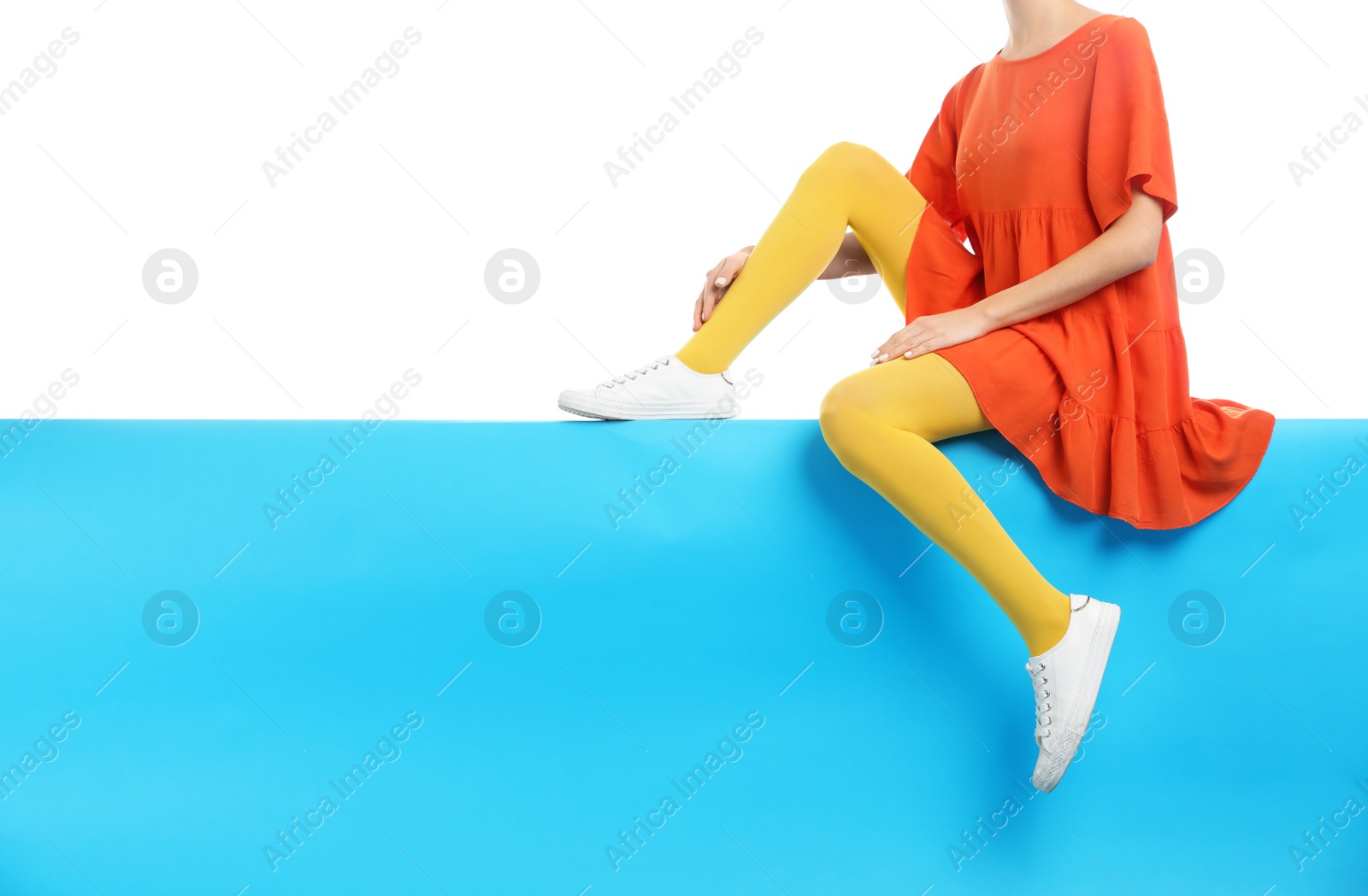 Photo of Woman wearing yellow tights and stylish shoes sitting on color background, closeup. Space for text