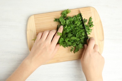 Photo of Woman cutting fresh green parsley on wooden board at table, top view