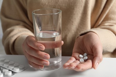 Woman with glass of water and pills at white table, closeup