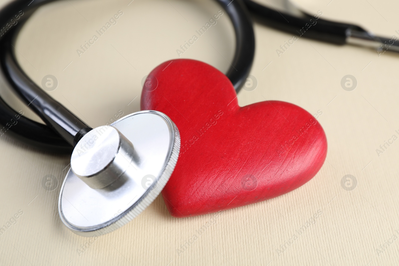 Photo of Stethoscope and red heart on beige background, closeup