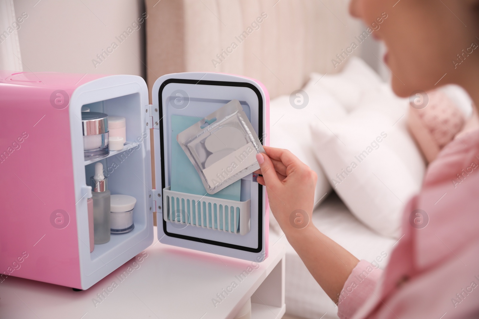 Photo of Woman taking eye patches out of cosmetic refrigerator indoors, closeup