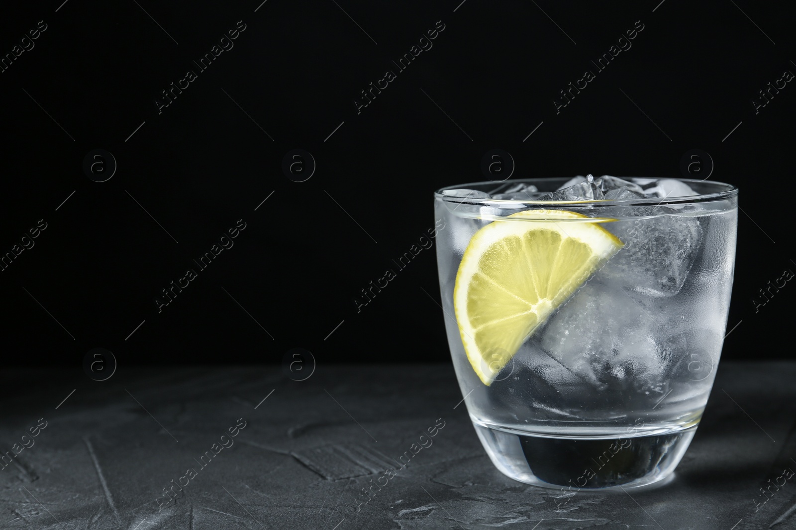 Photo of Water with ice cubes and lemon on grey table, closeup. Space for text