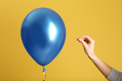 Woman piercing balloon with needle on color background, closeup