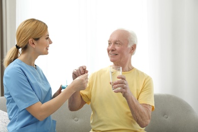 Nurse giving medication to elderly man indoors. Assisting senior people