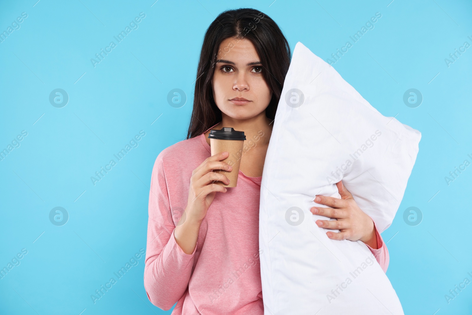 Photo of Tired young woman with soft pillow and cup of coffee on light blue background