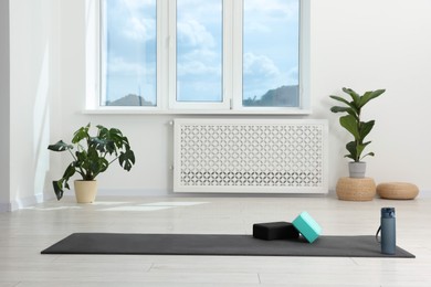 Photo of Exercise mat, yoga blocks and bottle of water on floor in room