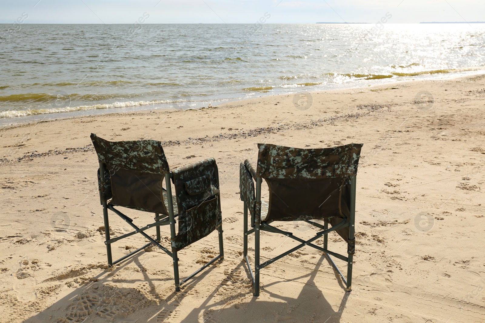 Photo of Comfortable camouflage fishing chairs on sandy beach near sea