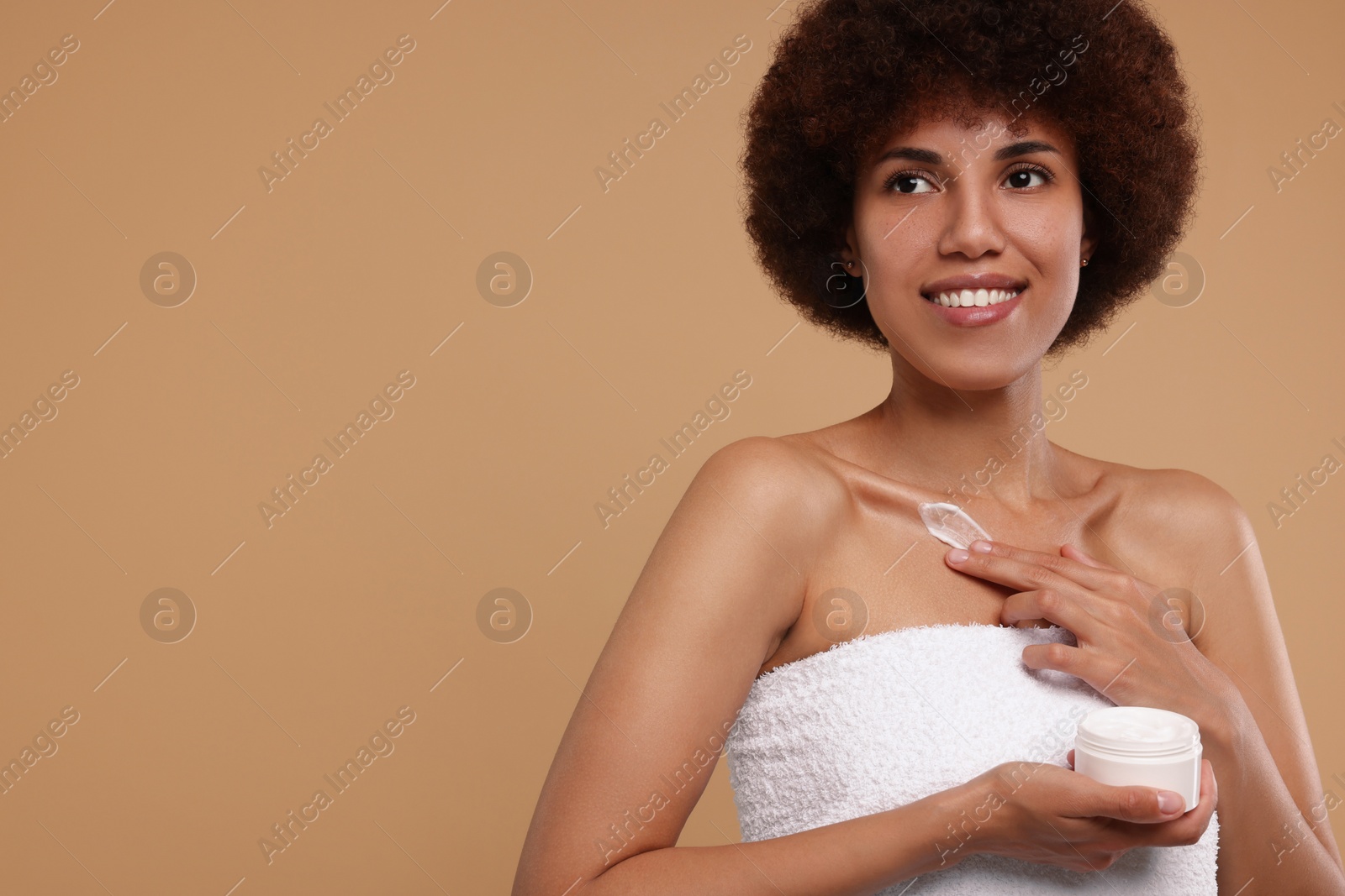 Photo of Beautiful young woman applying cream onto body on beige background, space for text