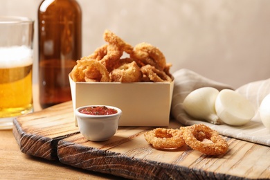 Photo of Cardboard box with crunchy fried onion rings and sauce on table