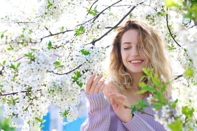 Photo of Attractive young woman posing near blossoming tree on sunny spring day