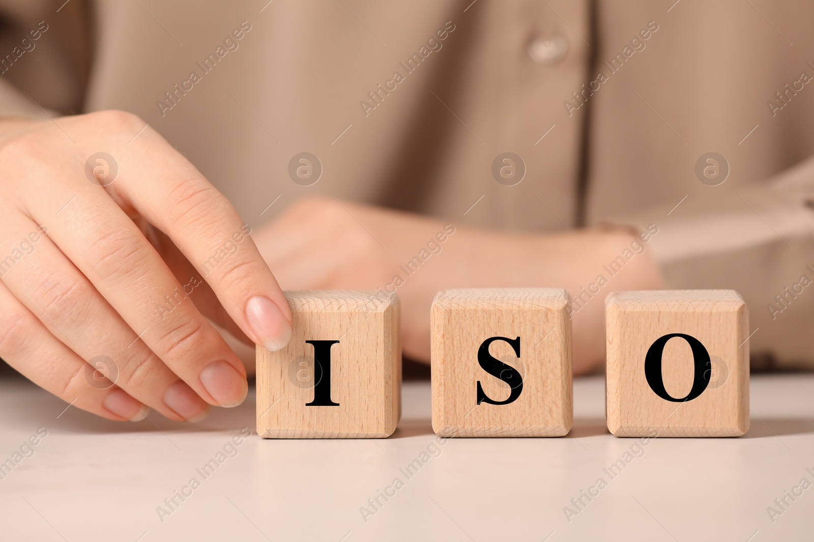 Photo of Woman making abbreviation ISO of wooden cubes at white table, closeup