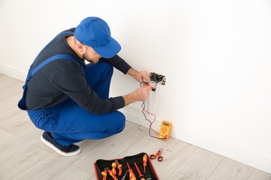 Electrician with tester checking voltage indoors, space for text