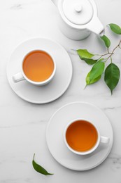 Photo of Green tea in cups with leaves and teapot on white marble table, flat lay