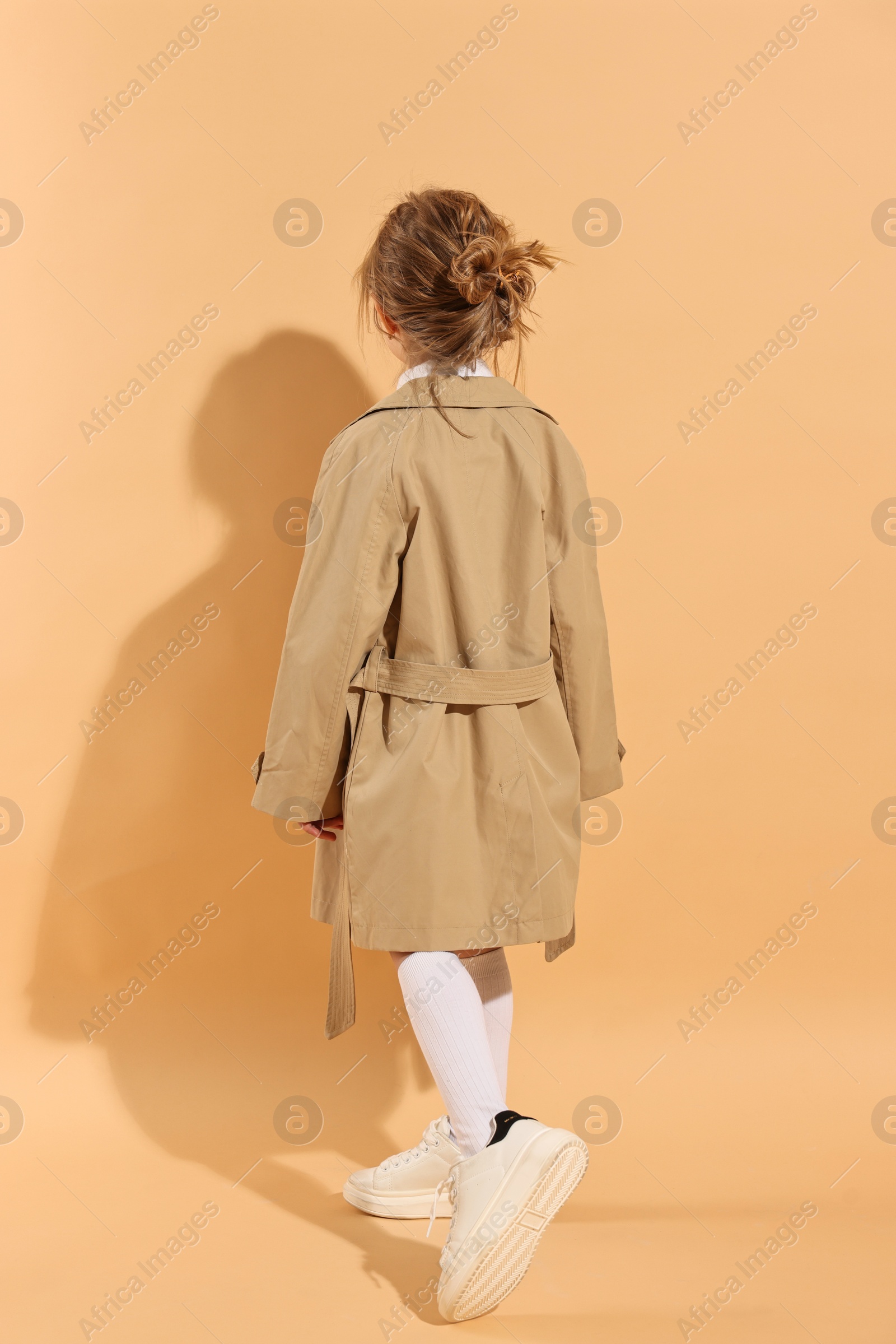 Photo of Fashion concept. Stylish girl posing on pale orange background, back view