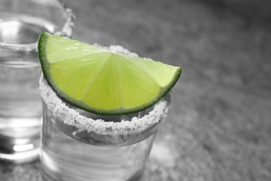 Photo of Mexican Tequila shot with salt and lime slice on grey table, closeup