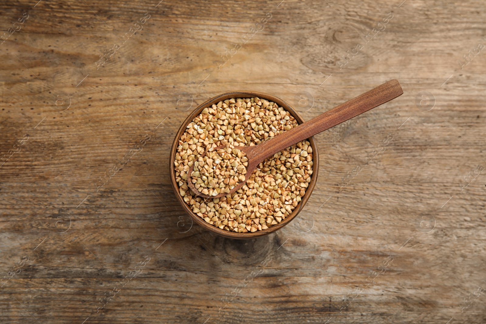 Photo of Uncooked green buckwheat grains in bowl on wooden table, top view