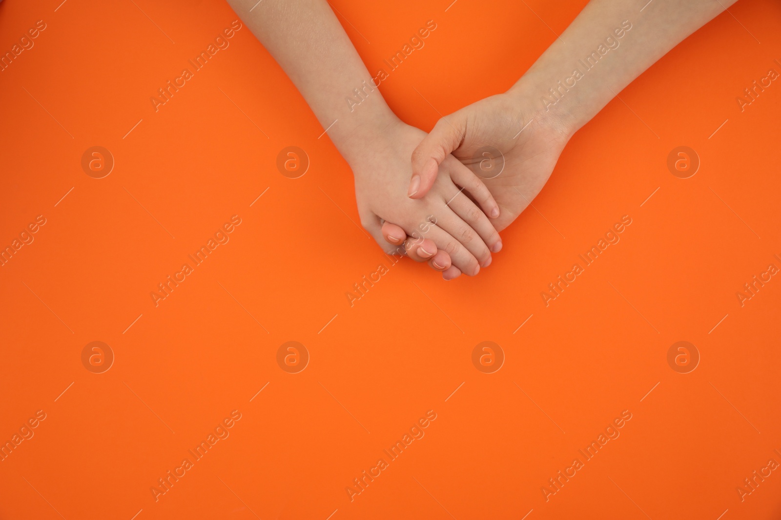 Photo of Mother holding hands with her child on orange background, top view. Happy family