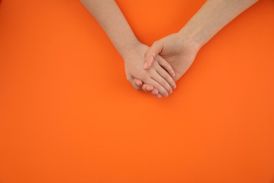 Photo of Mother holding hands with her child on orange background, top view. Happy family