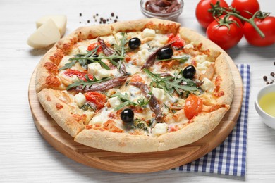 Tasty pizza with anchovies and ingredients on white wooden table