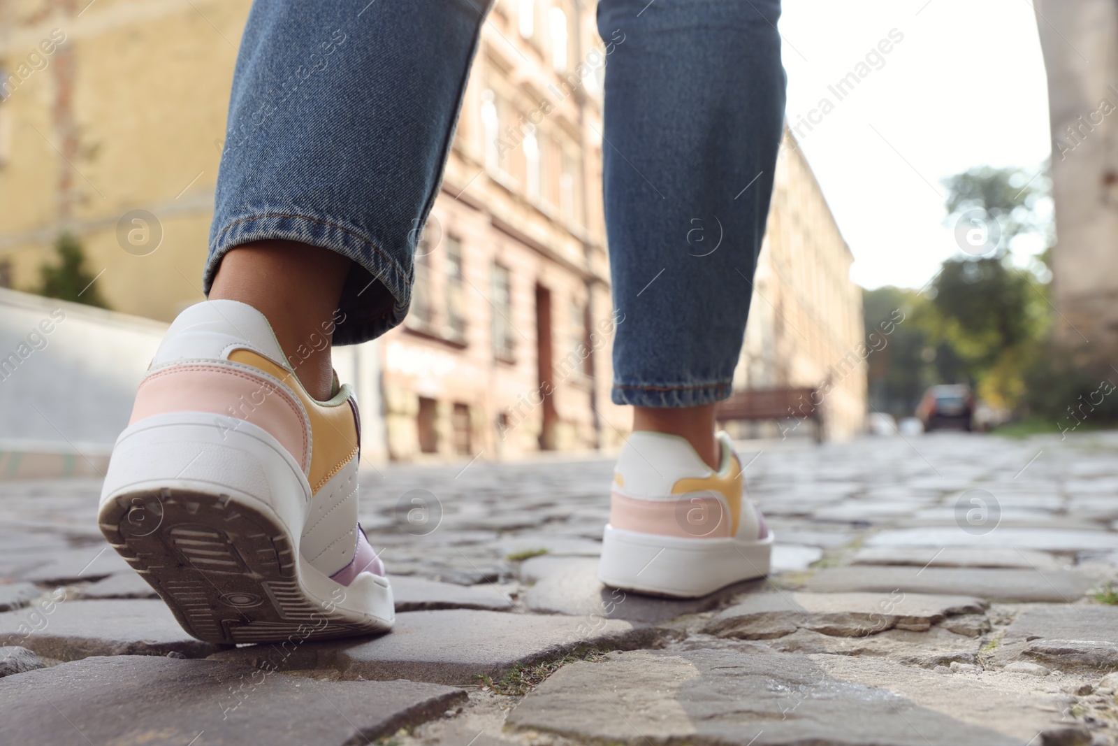 Photo of Woman in stylish sneakers walking on city street, closeup