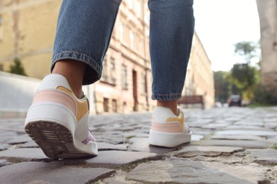 Photo of Woman in stylish sneakers walking on city street, closeup