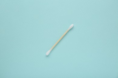 Photo of One wooden cotton bud on turquoise background, top view