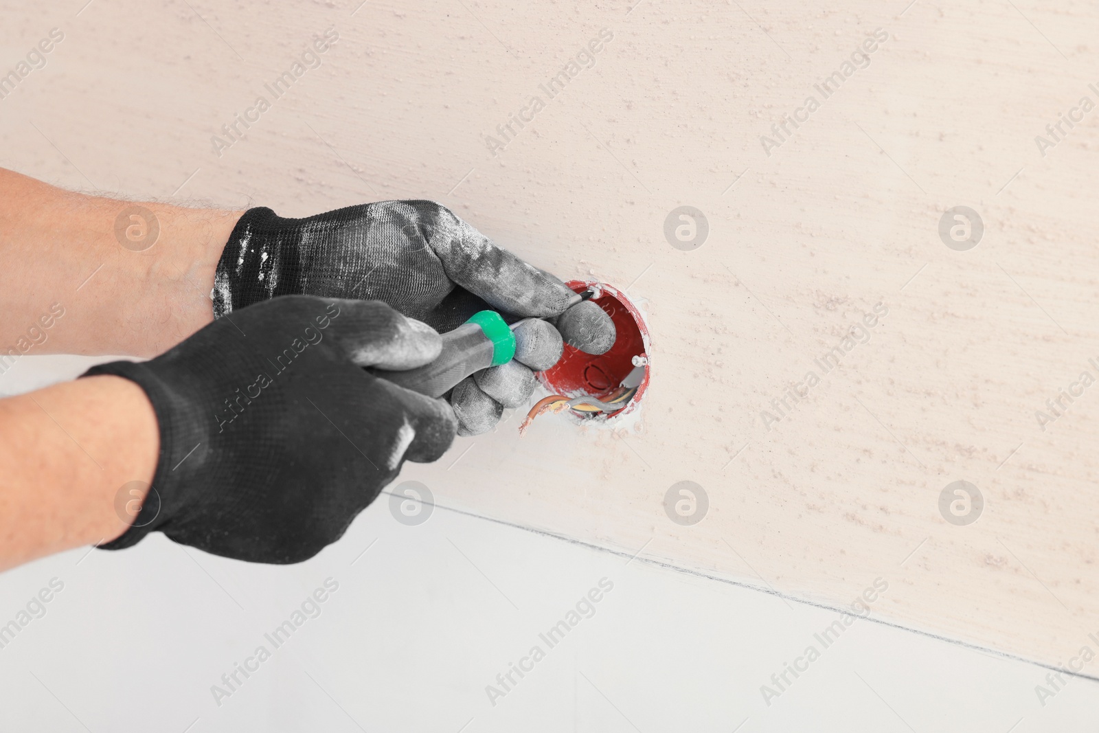 Photo of Electrician with screwdriver repairing power socket indoors, closeup. Space for text