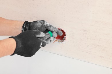 Photo of Electrician with screwdriver repairing power socket indoors, closeup. Space for text