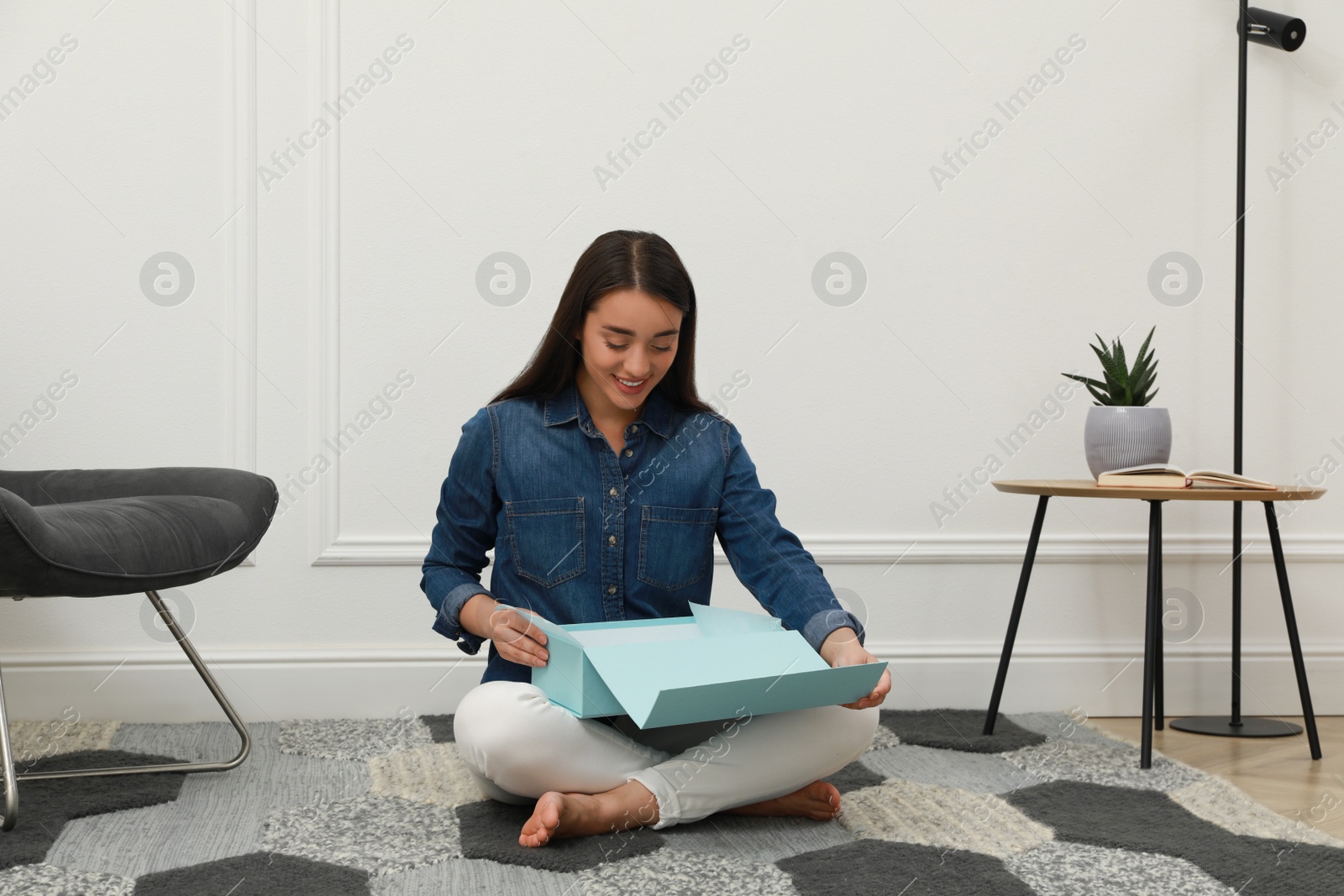 Photo of Happy young woman opening parcel at home. Internet shopping