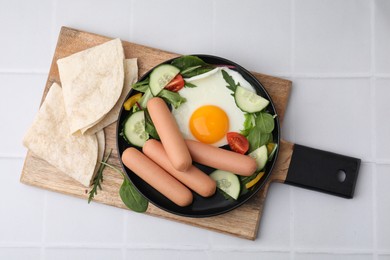 Delicious breakfast with boiled sausages and fried egg on white tiled table, top view