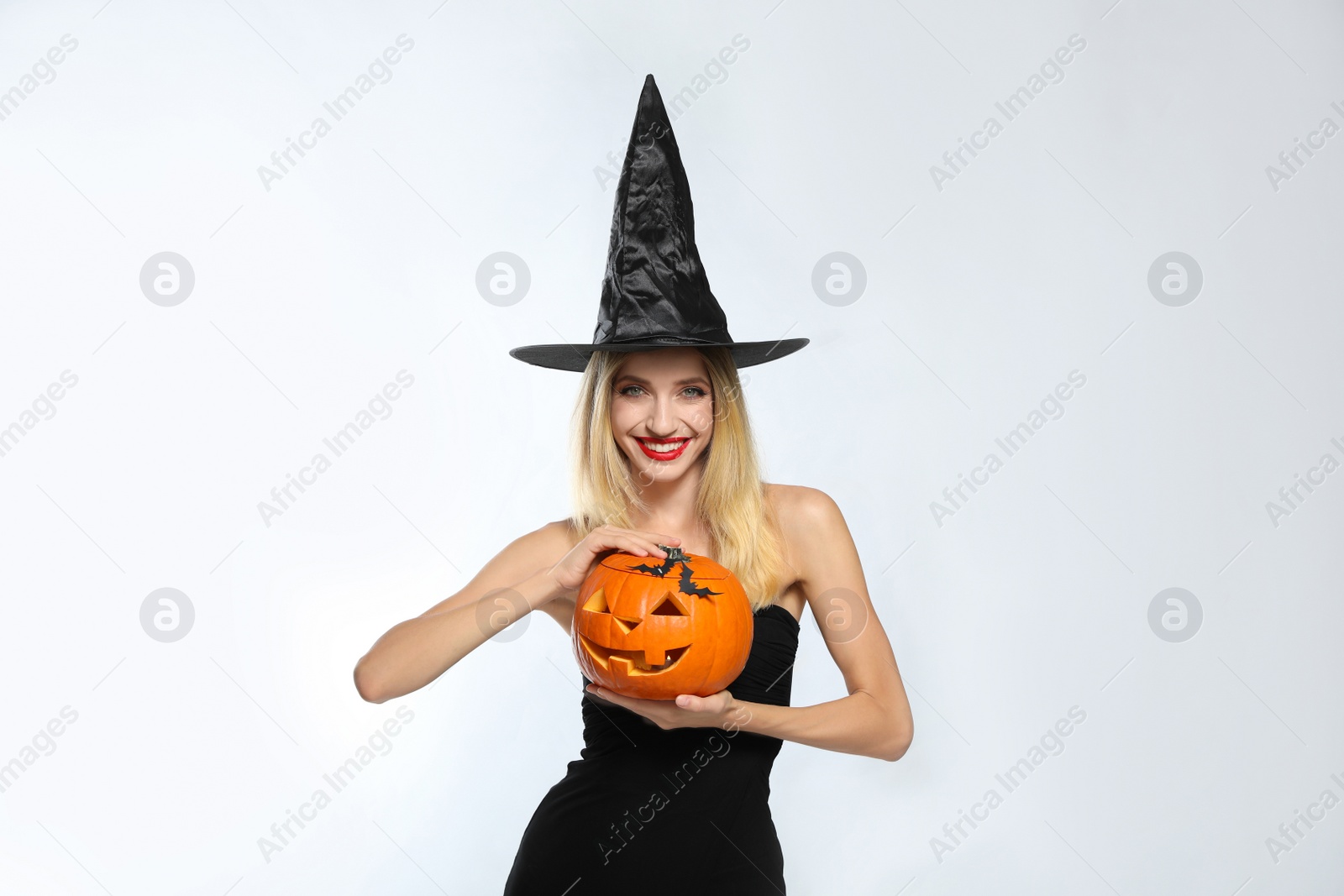 Photo of Beautiful woman in witch costume with jack o'lantern on white background. Halloween party