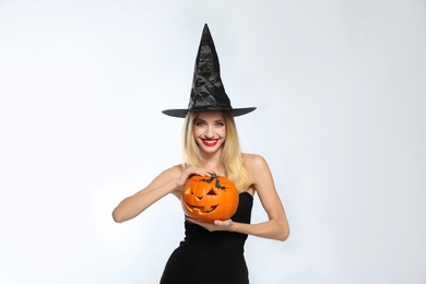 Beautiful woman in witch costume with jack o'lantern on white background. Halloween party