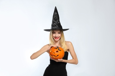 Photo of Beautiful woman in witch costume with jack o'lantern on white background. Halloween party