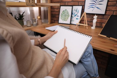Woman drawing in sketchbook with pencil at home, closeup