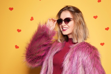 Photo of Beautiful young woman in fur coat with sunglasses posing on color background