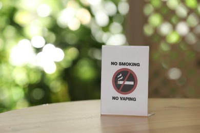 Photo of No Smoking No Vaping sign on wooden table against blurred background, space for text
