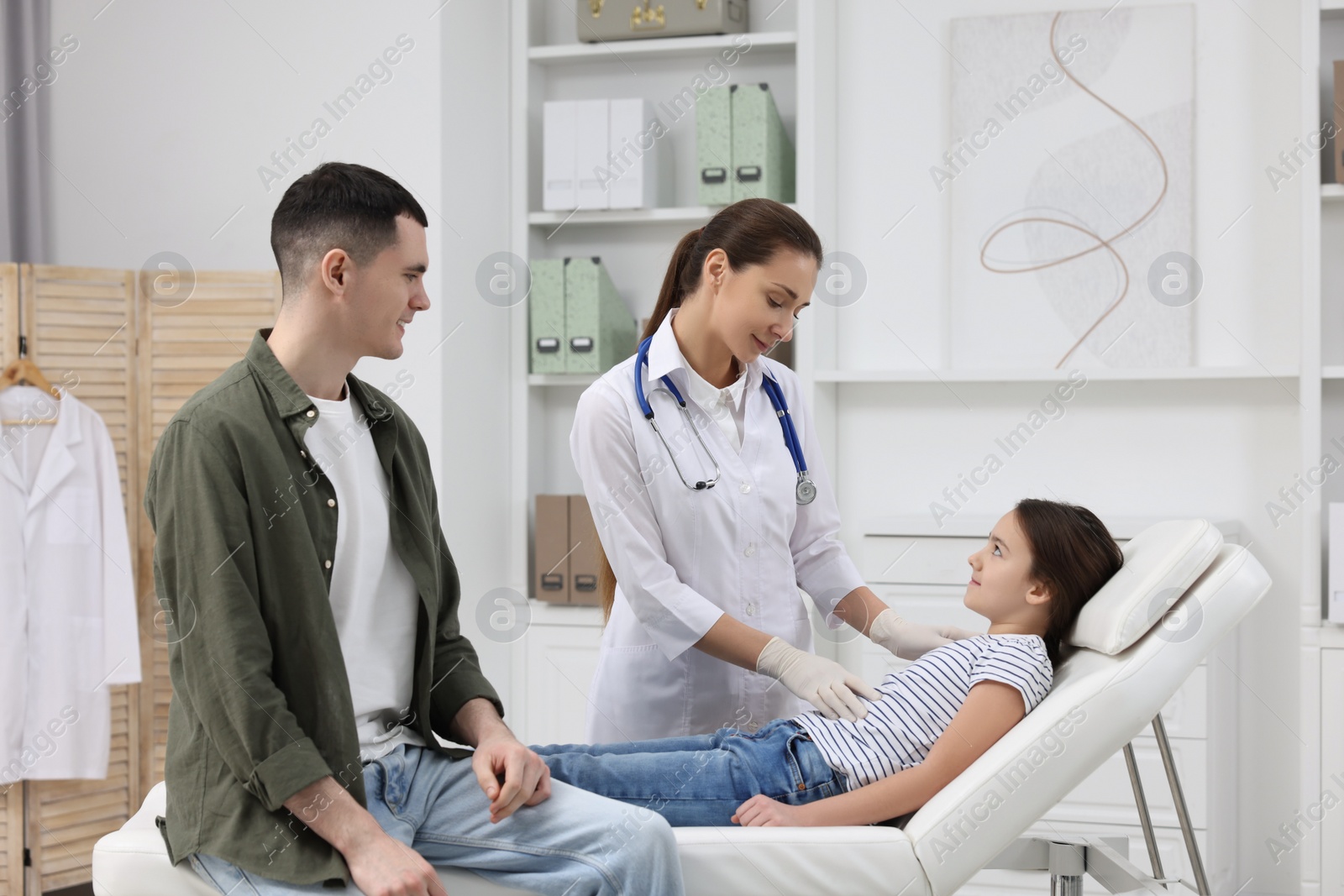 Photo of Gastroenterologist examining girl with stomach ache on couch in clinic