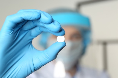 Photo of Scientist in protective gloves holding pill, focus on hand