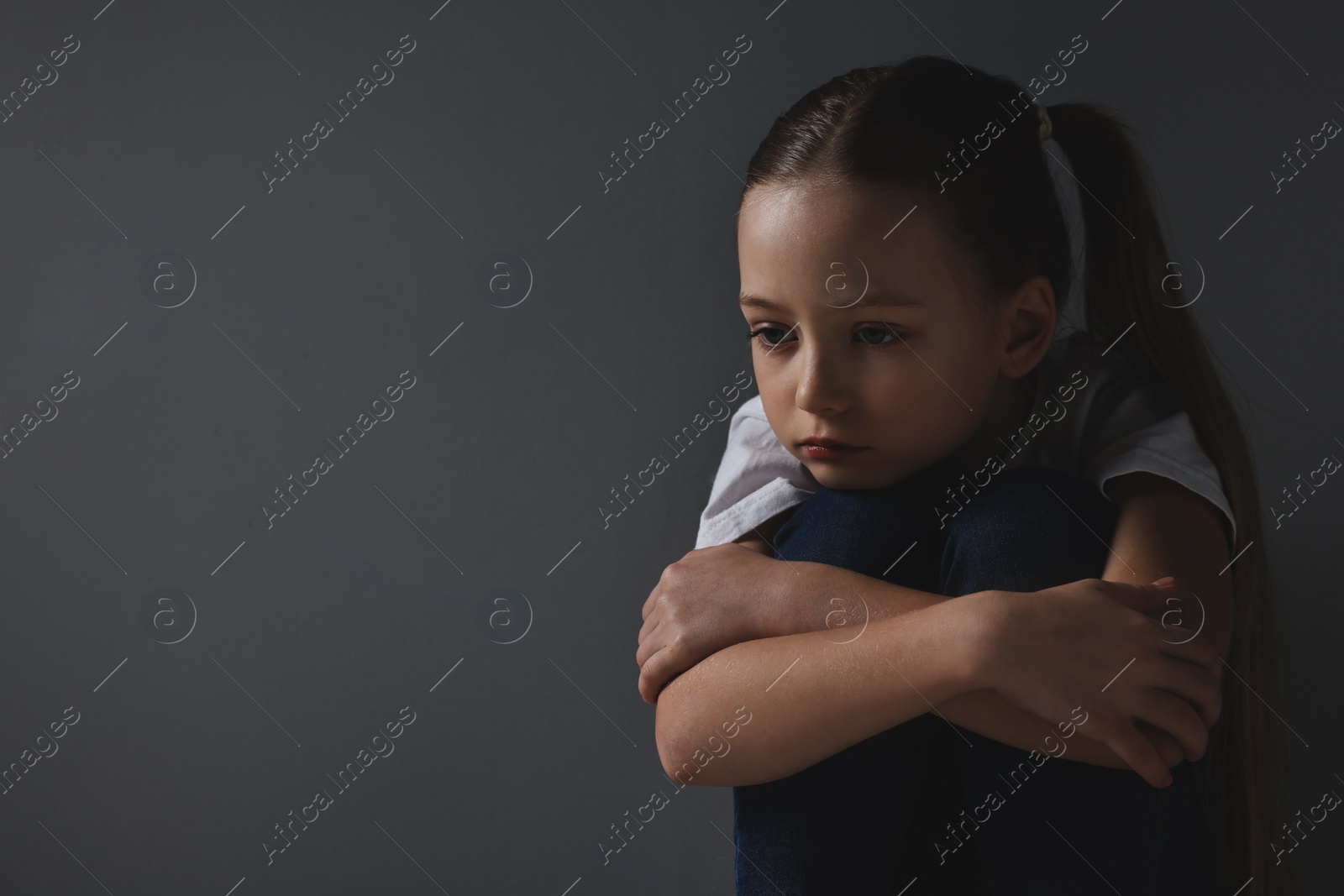 Photo of Sad girl sitting near dark grey background, space for text